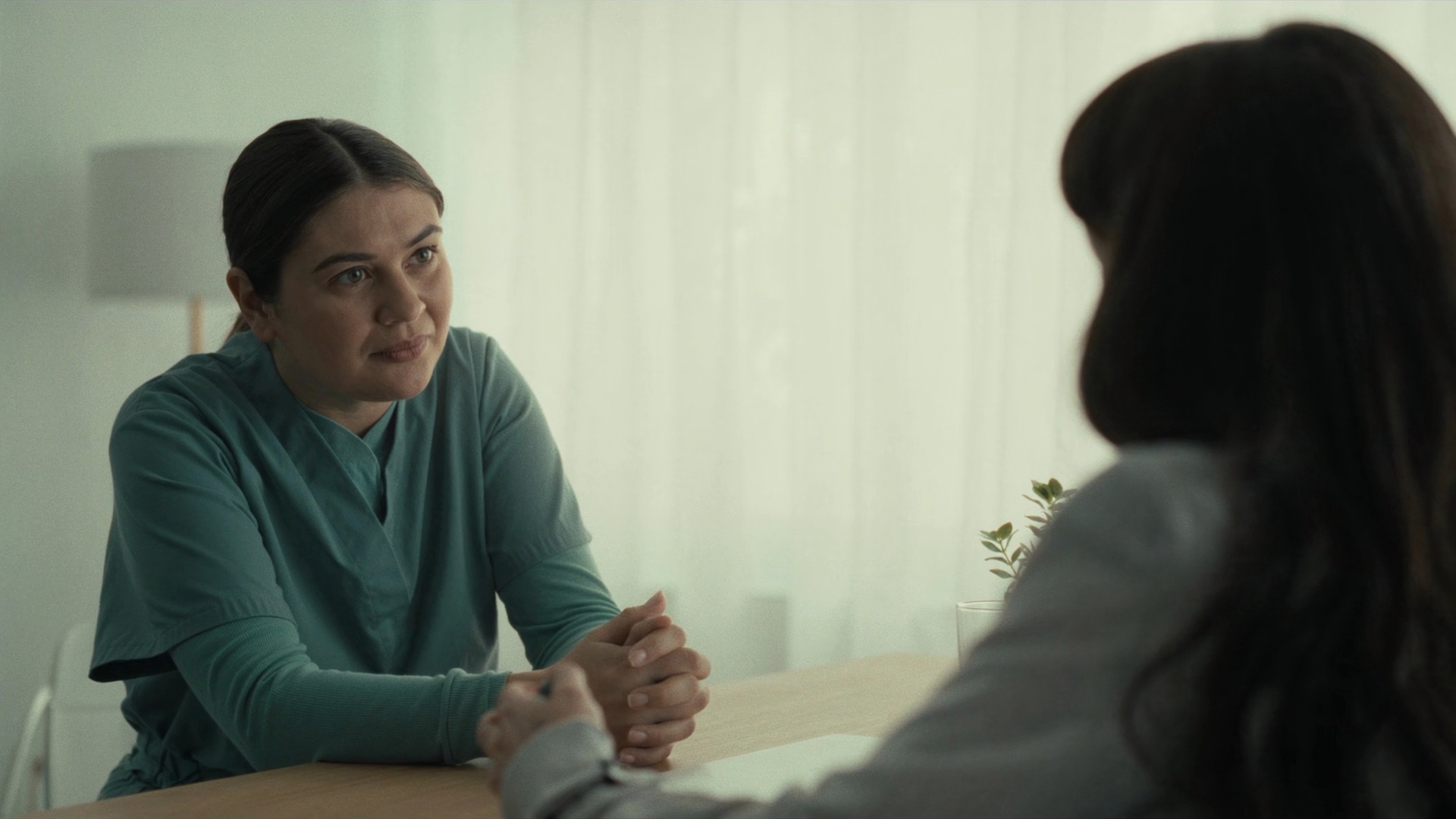 A doctor talks with a patient in a bright consultation room, the two of them seated at a light wood table, with no phones or screens between them.